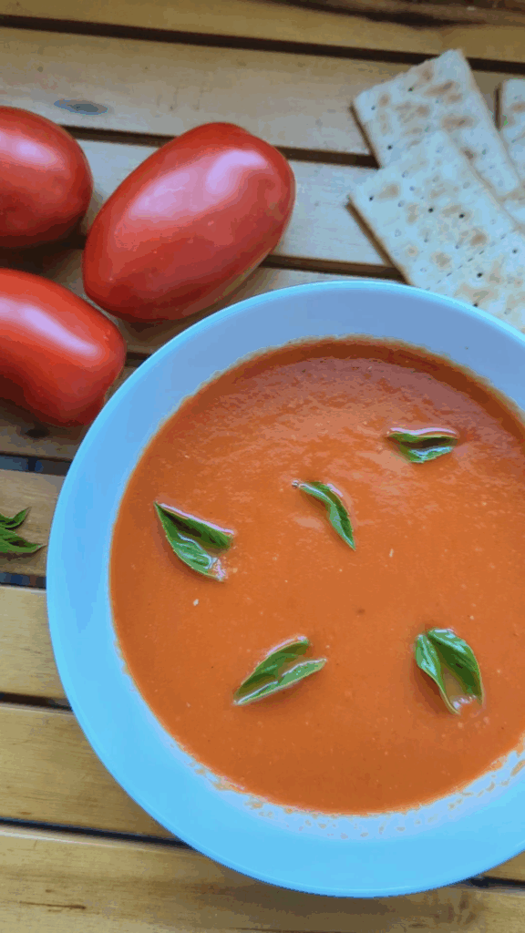 Bowl of homemade smoky roasted tomato soup garnished with fresh basil, made with roasted summer tomatoes, garlic, shallots, balsamic vinegar and thyme.