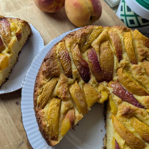 Golden peach polenta cake topped with fresh Ontario peach slices on a rustic wooden board.