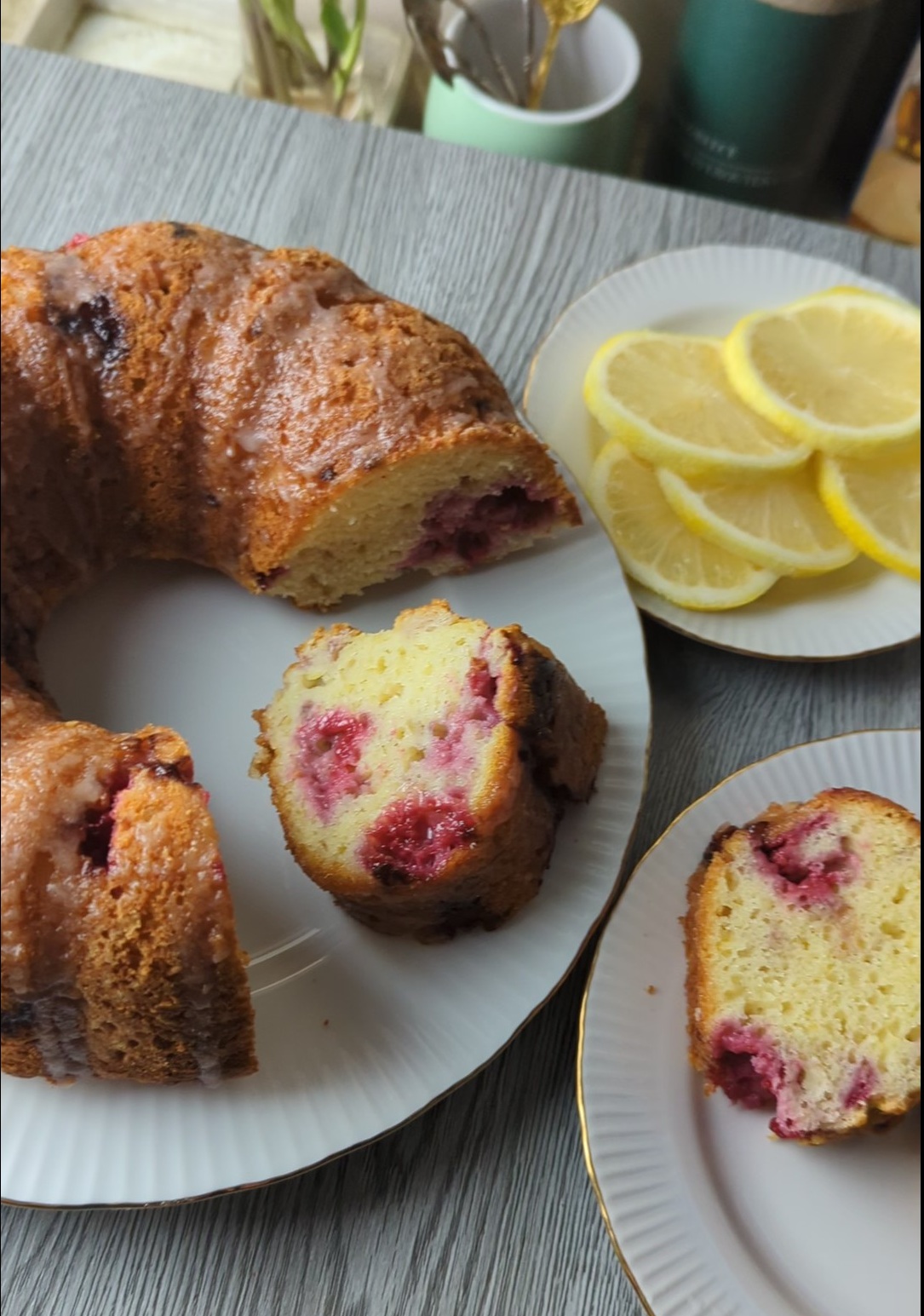 Lemon raspberry Greek yogurt Bundt cake sliced to show fresh raspberries throughout the tender crumb, with lemon slices on a plate beside it