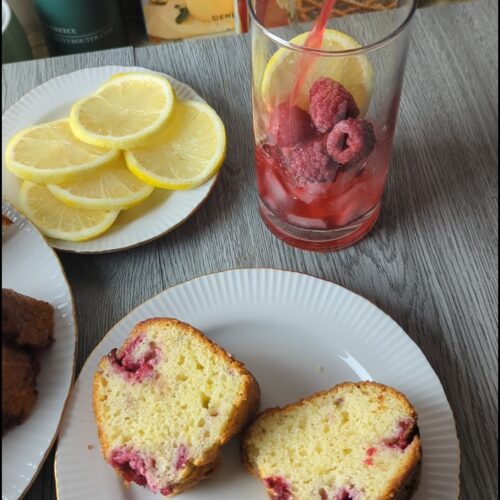 Lemon raspberry Greek yogurt Bundt cake sliced to show fresh raspberries throughout the tender crumb, with lemon slices on a plate beside it