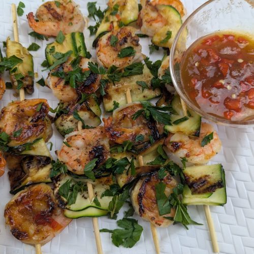Sweet and spicy apricot shrimp skewers with grilled zucchini ribbons and fresh mint on a hot grill pan.