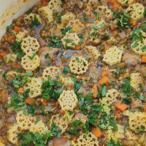A comforting bowl of winter lentil and sausage stew topped with grated parmesan cheese and served next to optional chili oil.
