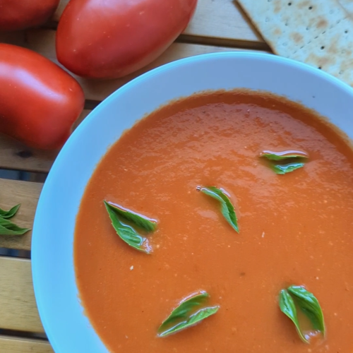 Bowl of homemade smoky roasted tomato soup garnished with fresh basil, made with roasted summer tomatoes, garlic, shallots, balsamic vinegar and thyme.