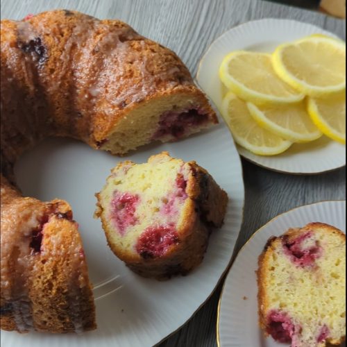 Lemon raspberry Greek yogurt Bundt cake sliced to show fresh raspberries throughout the tender crumb, with lemon slices on a plate beside it